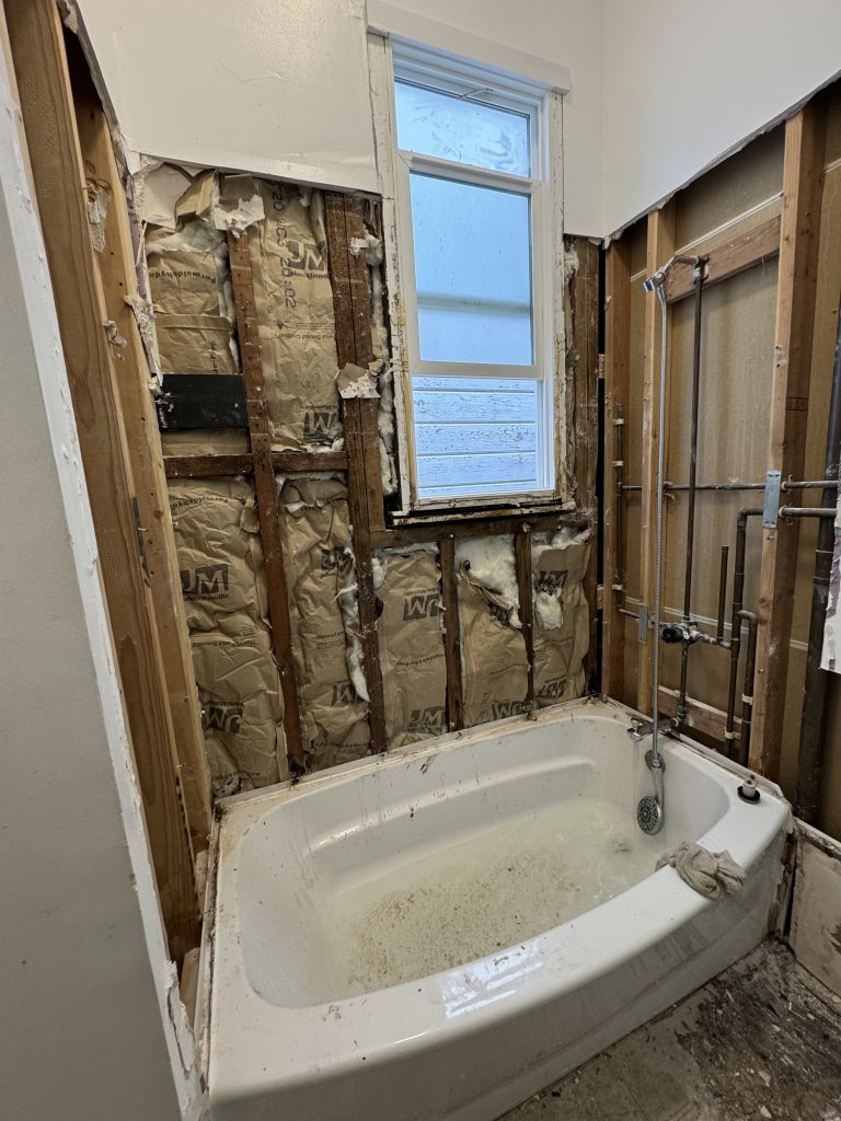 Demolished bathroom in San Ramon, exposing wall studs with insulation and plumbing around a dirty bathtub.